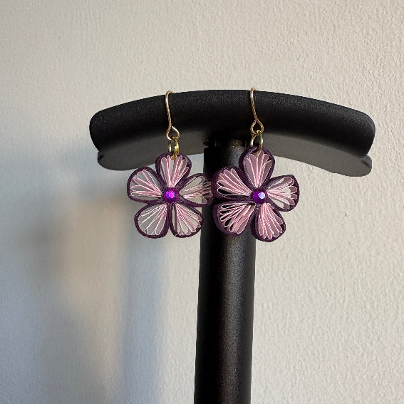 Flower-shaped earrings on a black stand against a light background