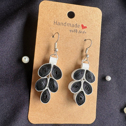 Pair of black and white quilled earrings on a 'Handmade with Love' card against a dark fabric background.
