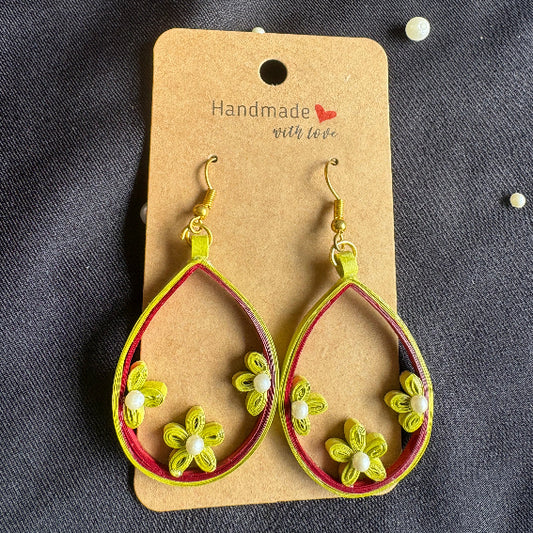 Pair of yellow hoop earrings with floral designs on a 'Handmade' card against a dark fabric background.