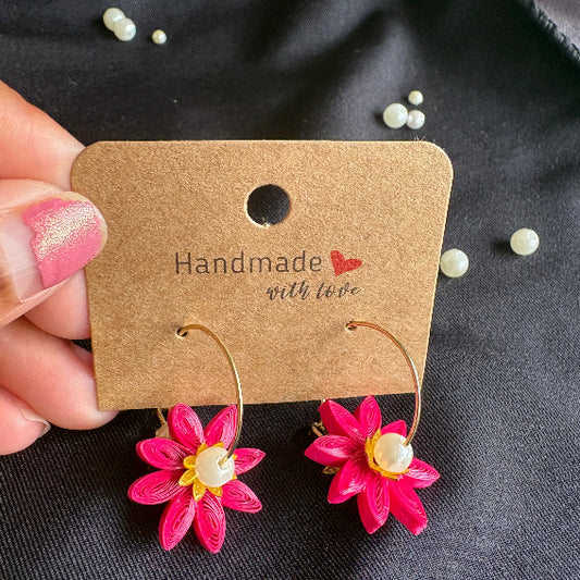 Handmade flower-shaped earrings on a black fabric background with a brown label.