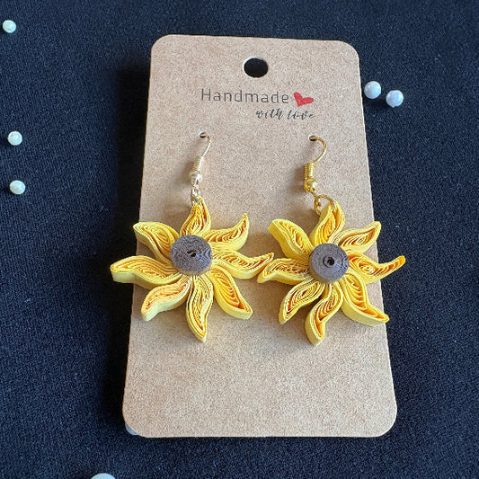 Gold sunflower earrings on a cardboard backing with 'handmade' label against a dark background.
