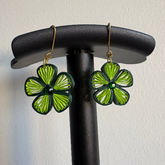 Green flower-shaped earrings on a black stand against a light background