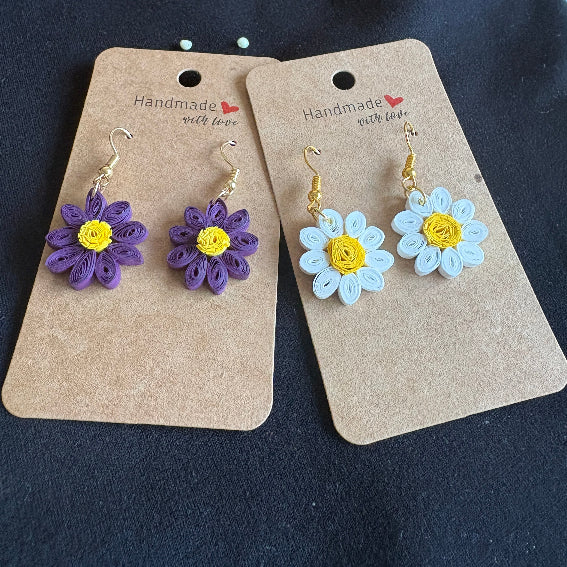 Flower-shaped earrings on cardboard cards against a dark background