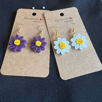 Flower-shaped earrings on cardboard cards against a dark background