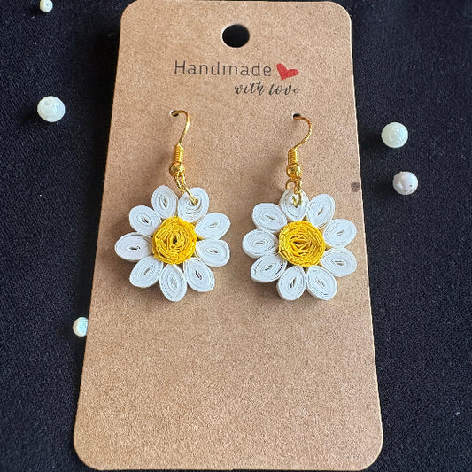 Pair of white flower-shaped earrings with gold centers on a brown card against a dark background.