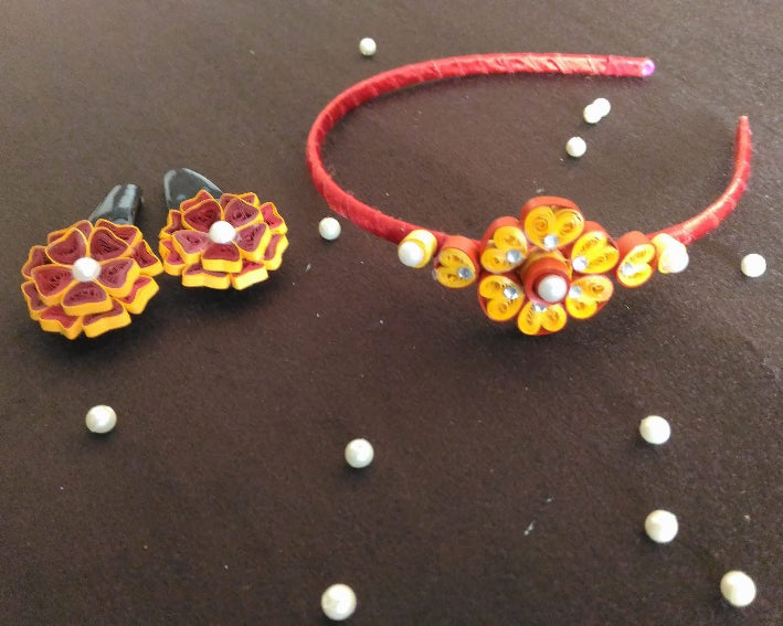 Decorative headband and earrings with floral designs on a brown surface.