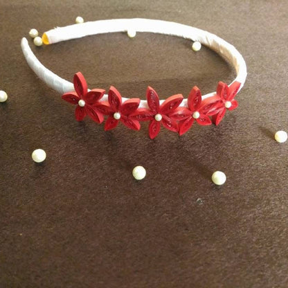 White headband with red floral decorations and small white beads on a brown surface